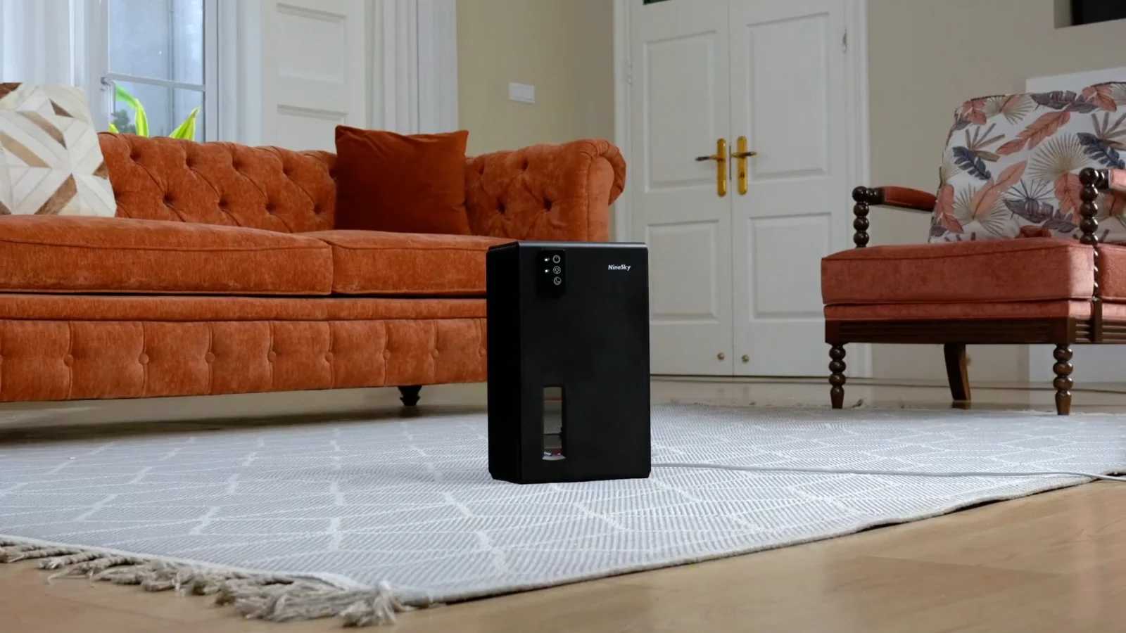 A black NineSky CT2 working in a living room with an orange sofa